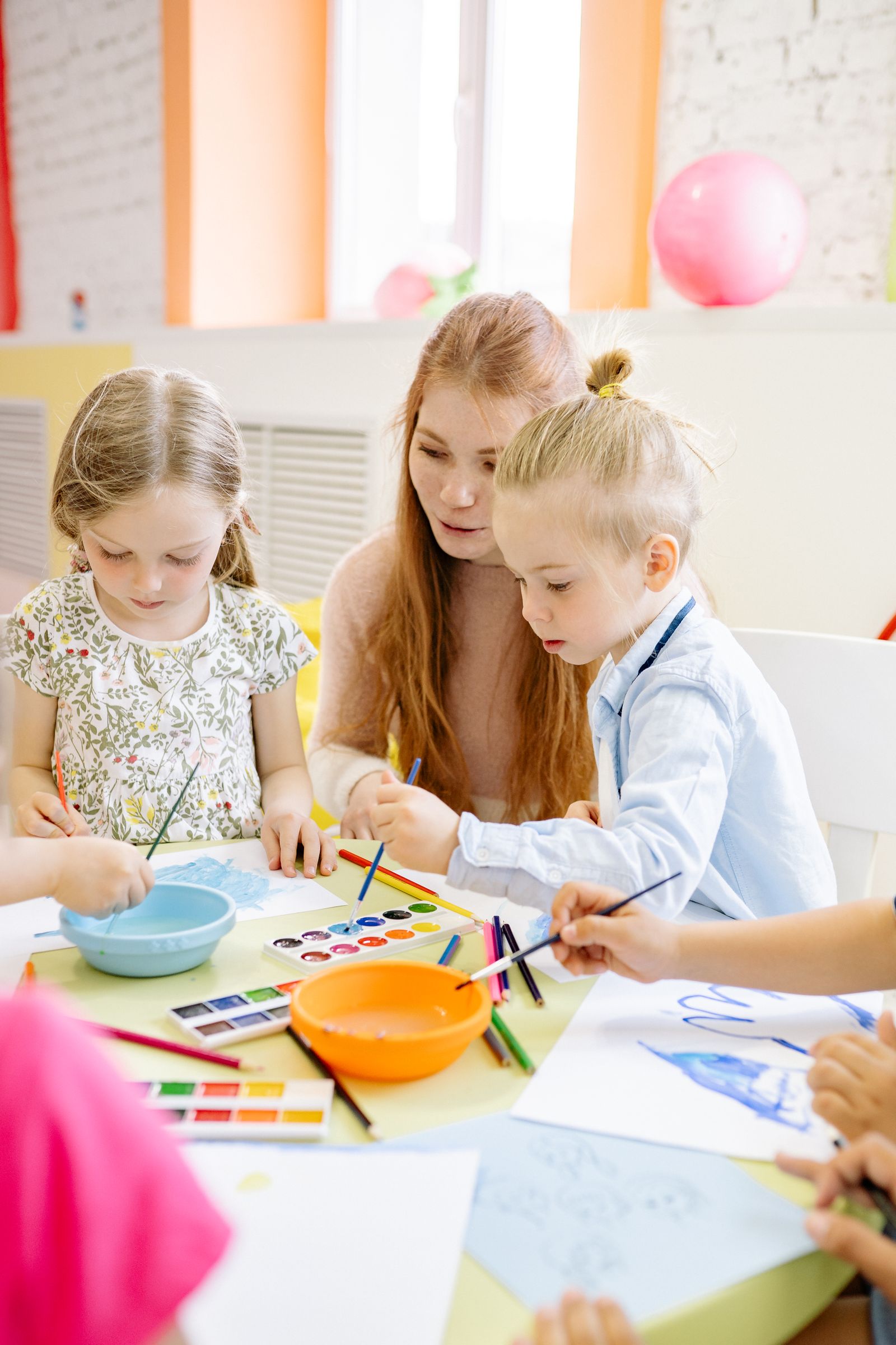 Pädagogische Fachkraft begleitet zwei Kinder beim Malen mit Wasserfarben im hauseigenen Atelier