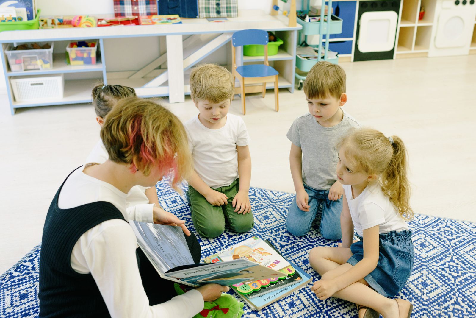 Pädagogische Fachkraft liest einer Gruppe von Kindern gemeinsam ein Buch vor