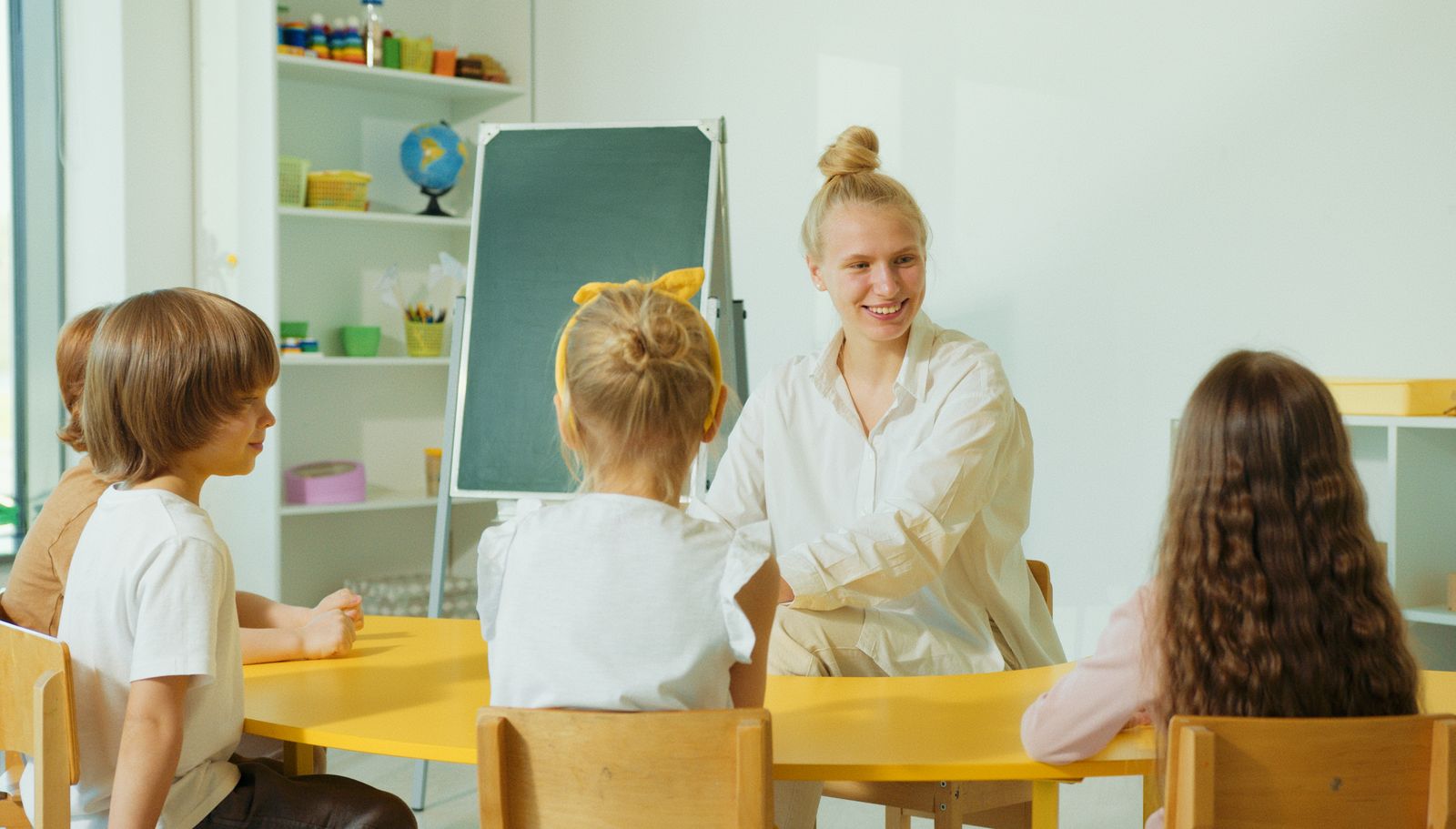 Pädagogische Fachkraft im Austausch mit Kindern in einem hellen Gruppenraum
